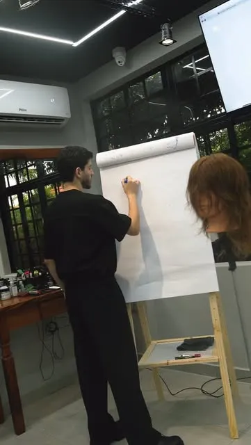 Profissional escrevendo num flip-chart durante treinamento da equipe dentro da barbearia